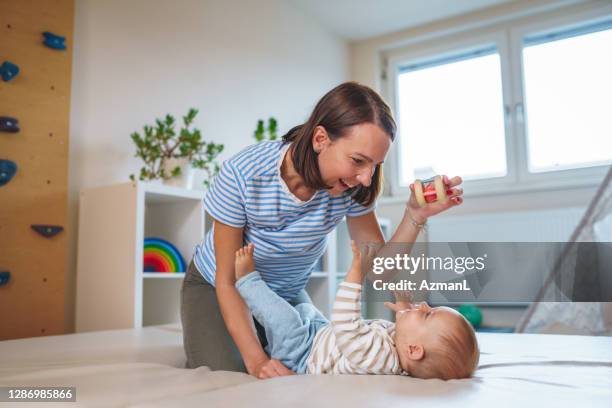 happy caucasian mother playing with baby boy in playroom at home - baby rattle stock pictures, royalty-free photos & images