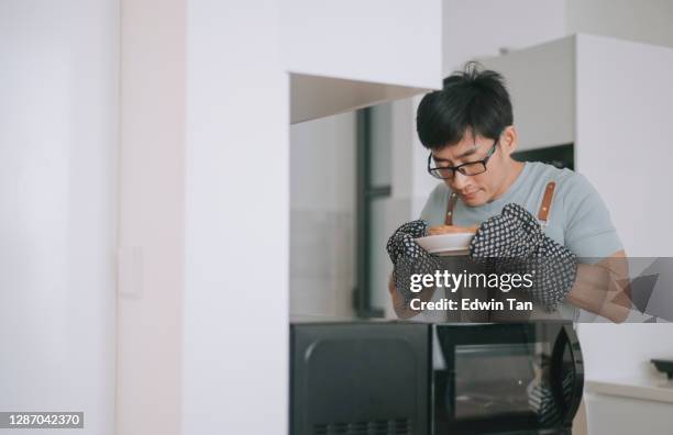 homme asiatique chinois obtenant sa tarte hors du micro-ondes utilisant le gant protecteur dans sa cuisine - microwave photos et images de collection