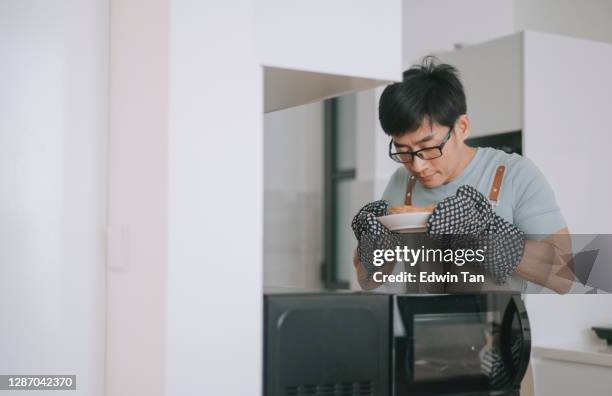 chinese asian man getting his pie out from microwave using protective glove in his kitchen - man microwave stock pictures, royalty-free photos & images