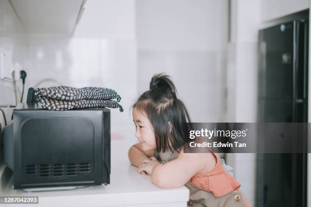 young asian chinese girl waiting and looking her food out from microwave using protective glove in kitchen - microwave cooking stock pictures, royalty-free photos & images