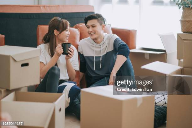 リビングルームの引っ越し家でカートン段ボール箱を開けた後、床に座っているアジアの中国人カップル - 賃借人 ストックフォトと画像