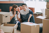 asia chinese couple sitting on floor resting after opening carton cardboard boxes in living room moving house