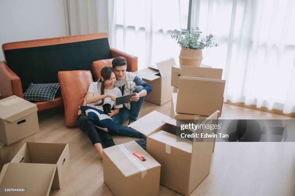 Asia chinese couple sitting on floor resting after opening carton cardboard boxes in living room moving house