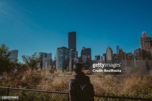a man with a backpack on his back with the view of the manhattan buildings in new york city - backpacker apartment stock pictures, royalty-free photos & images