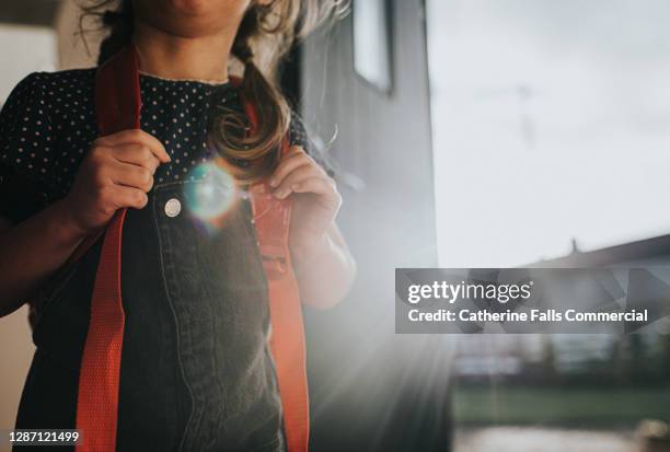 little girl wears a backpack in a sunny environment - focus is on her gripping the straps on her shoulders - leaving school imagens e fotografias de stock