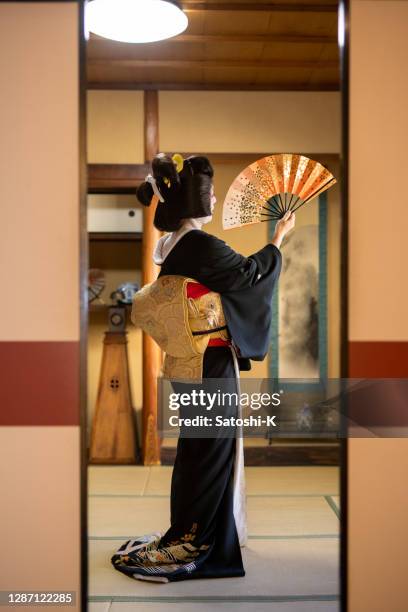 femme japonaise de geisha dans la danse noire et d’or de kimono avec le ventilateur pliant de papier dans la salle japonaise de tatami - kimono photos et images de collection