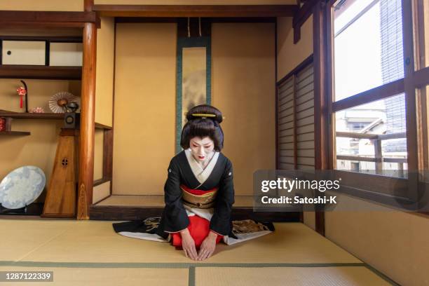 japanische geisha frau in schwarz und gold kimono sitzen in 'washitsu' japanischen zimmer und gruß - geisha stock-fotos und bilder