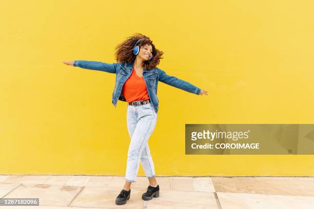 young woman with african roots and curly hair dancing and listening to music with headphones - stock photo - escutando - fotografias e filmes do acervo