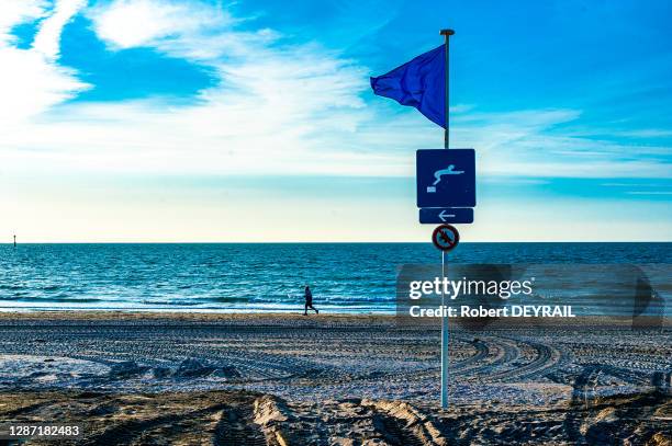 Panneau et drapeau de surveillance de la baignade et homme courant sur la plage le 10 avril 2014 à Trouville, France.