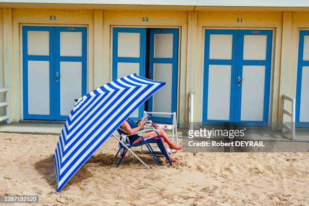 Une estivante devant sa cabine de bain lit un magazine assise sur un fauteuil de plage protégée du soleil par un parasol le 13 juillet 2014 à...