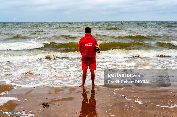 Maître nageur sauveteur-secouriste en tenue rouge tenant ses palmes sur la plage par mauvais temps le 12 juillet 2014 à Trouville, France.