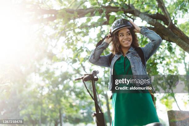 glückliche junge frau steht draußen und setzt helm - sports helmet stock-fotos und bilder