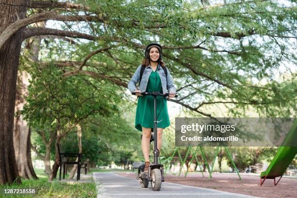 happy young woman riding motorized scooter outside - electric push scooter stock pictures, royalty-free photos & images