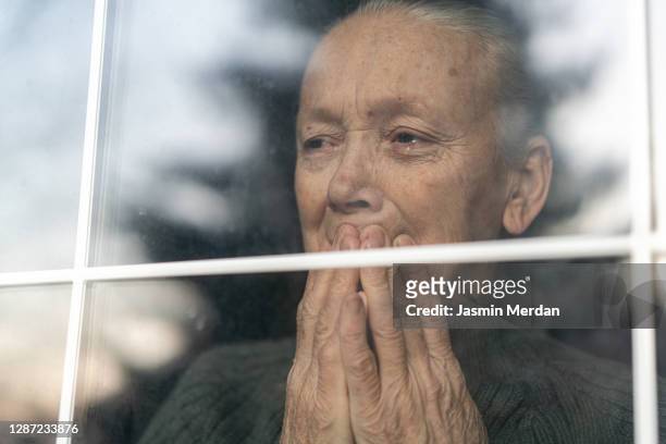 old woman in tears behind window indoors - sad old man fotografías e imágenes de stock