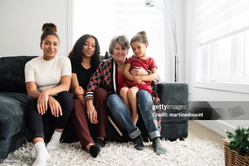 Mixed-race portrait of grandmother and granddaughters in living room.