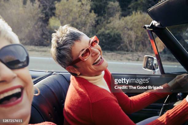 happy mature women driving in convertible car - lachen stockfoto's en -beelden