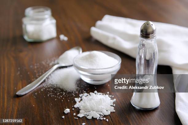 natural, organic, sea, white salt in a spoon, in a cup, in a salt shaker, poured on a wooden table. next to the linen towel. the concept of cooking healthy food, cosmetology. selective focus - salt shaker fotografías e imágenes de stock
