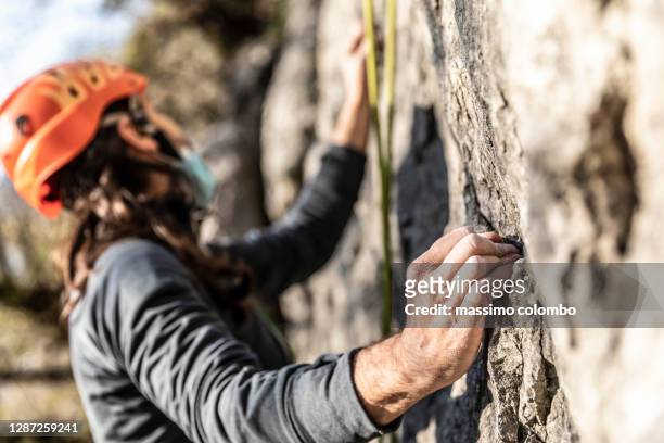 detail of climbers hand while moving up on rock wall - klettern stock-fotos und bilder