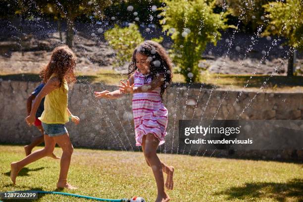 menina pulando sobre aspersão no jardim com amigos - aspersor - fotografias e filmes do acervo