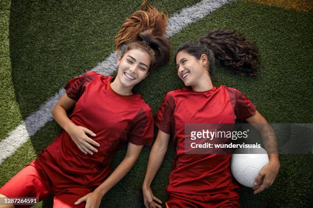 zwei glückliche fußball-teamkolleginnen entspannen auf dem rasen liegend - strip stock-fotos und bilder