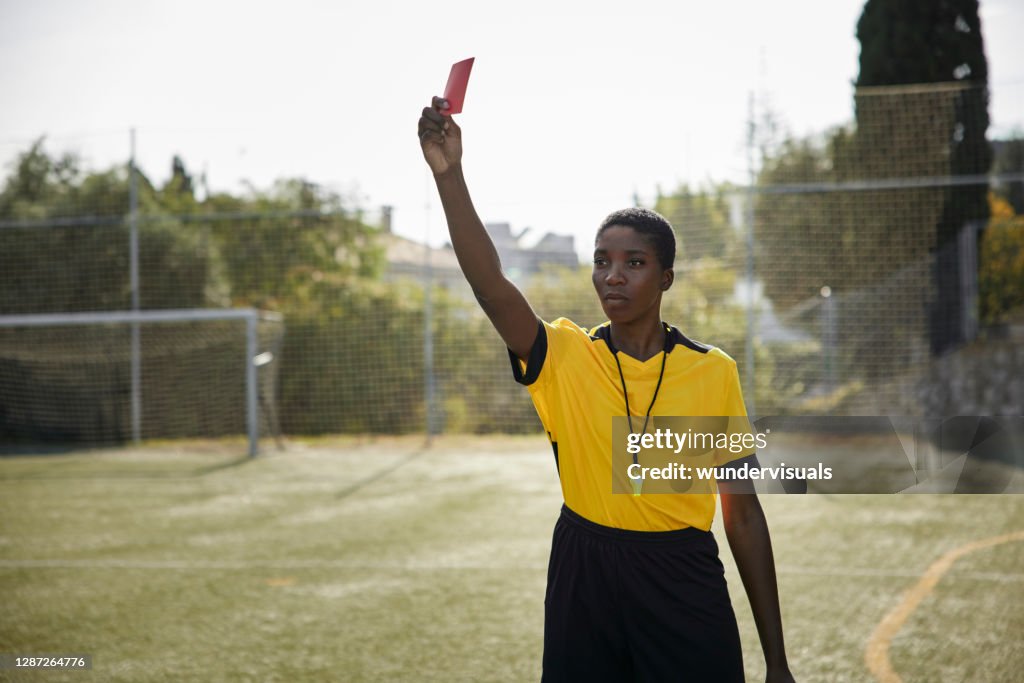 Arbitro mujer afroamericana sosteniendo tarjeta roja en uniforme amarillo