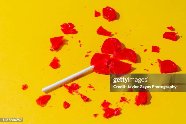 broken red heart-shaped lollipop on yellow background - fim-de-relacionamento - fotografias e filmes do acervo