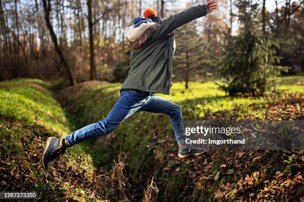 boy jumping over ditch in autumn forest - leap of faith stock pictures, royalty-free photos & images