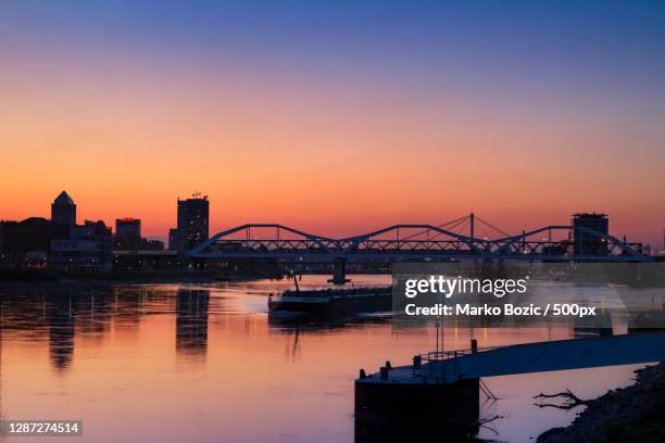 silhouette of bridge over river against sky during sunset,mannheim,germany - mannheim stock-fotos und bilder