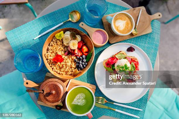 healthy breakfast with granola, fresh fruits, waffle with salmon and egg, matcha latte and cappuccino, high angle view - fruit smoothie instagram stock-fotos und bilder