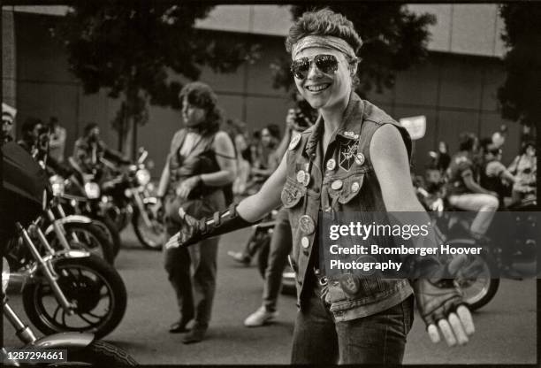 Portrait of smiling woman, dressed in a sleeveless denim jacket and fingerless gloves, from the 'Dykes on Bikes' group as she spreads out her hands...