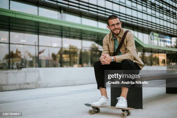 portrait of a casually dressed man is seating on bench in front of modern office. - modern malta stock pictures, royalty-free photos & images