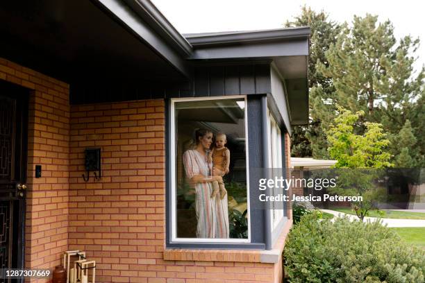 mother with baby son (18-23 months) standing behind window - blick durchs fenster aussenaufnahme haus stock-fotos und bilder