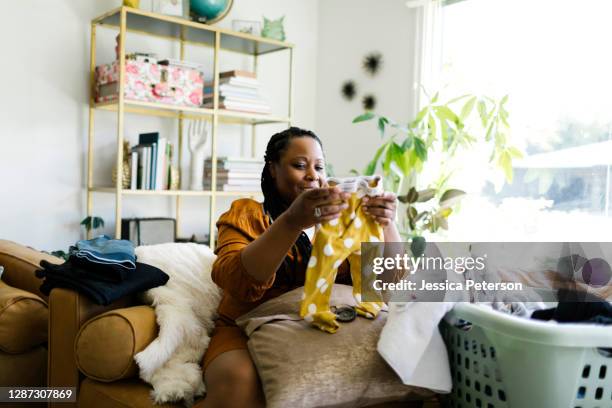 woman folding laundry in living room - baby clothes stock pictures, royalty-free photos & images