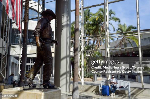 Traveler relaxes by the John Wayne statue at John Wayne Airport in Santa Ana, CA, on Monday, November 23, 2020.