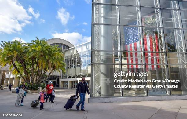 Travelers walk by the John Wayne statue at John Wayne Airport in Santa Ana, CA, on Monday, November 23, 2020.