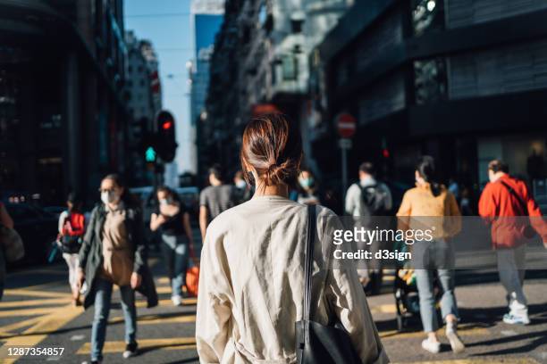 rear view of young asian woman commuting to work in city in the fresh morning, crossing street amidst crowd of pedestrians. daily life and routine of a businesswoman - hauptverkehrszeit stock-fotos und bilder