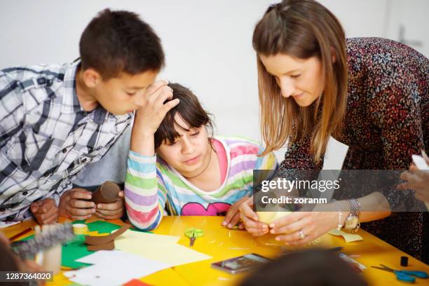special education teacher assisting intellectually disabled students in art class - special education stock pictures, royalty-free photos & images