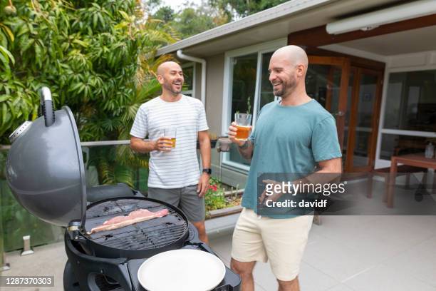 gay mannen koken een gas bbq thuis samen - completely bald stockfoto's en -beelden