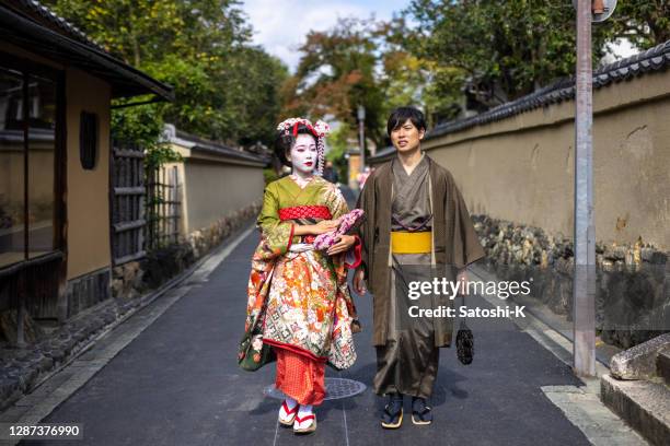 maiko (geisha in training) and a young man in 'hakama' kimono walking on street in gion, kyoto - geisha stock pictures, royalty-free photos & images