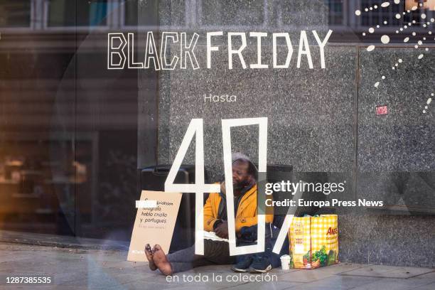 Homeless person sitting next to an establishment with 'Black Friday' discount signs in a shop on a central street in Madrid, on November 23 in...