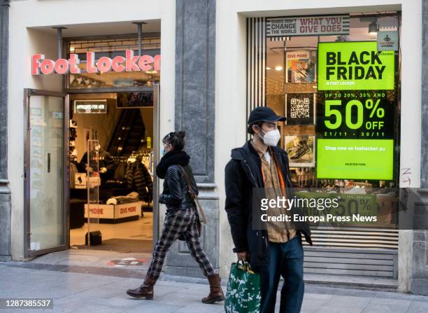 Passers-by walk next to an establishment with 'Black Friday' discount signs in a shop on a central street in Madrid, on November 23 in Madrid, Spain....