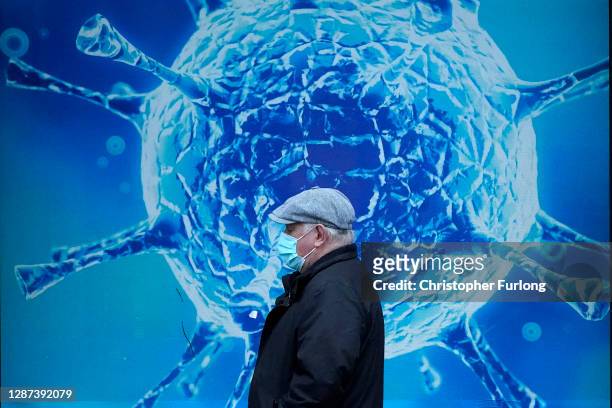 Man wearing a protective face mask walks past an illustration of a virus outside Oldham Regional Science Centre on November 24, 2020 in Oldham,...