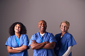 Studio Portrait Of Three Members Of Surgical Team Wearing Scrubs Standing Against Grey Background