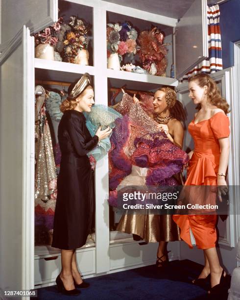 Brazilian singer and dancer Carmen Miranda shows her costumes to two young actresses, circa 1945.