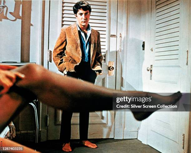 American actor Dustin Hoffman as Benjamin Braddock, watching his older lover Mrs Robinson get dressed in a promotional still from the film 'The...