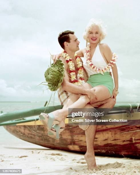 American actress Mamie Van Doren boses on a beach with a young man, circa 1958.