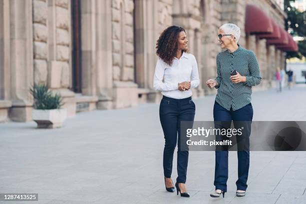 businesswomen walking side by side on the street - talking stock pictures, royalty-free photos & images