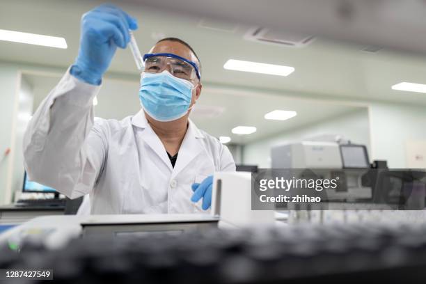 male doctor in medical laboratory looking at test tube in hand - medical lab stock pictures, royalty-free photos & images