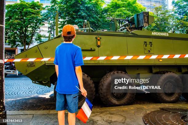 Jeune garçon tenant un drapeau français à la main, regarde un véhicule blindé de l'armée belge lors du défilé militaire sur les Champs Elysées le 14...