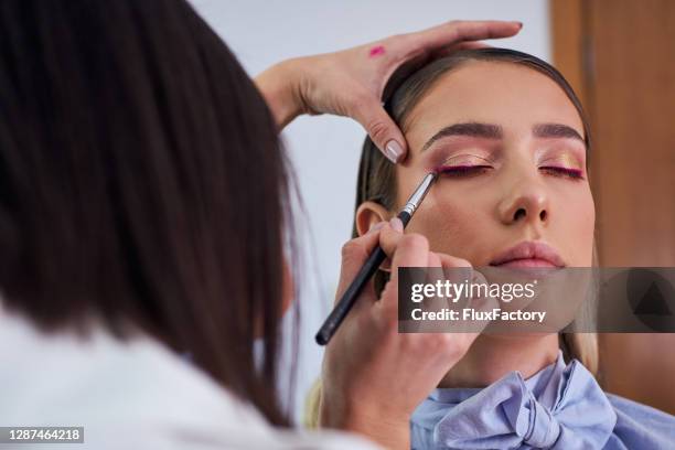 precise makeup artist using a thin eye liner brush to apply a purple eyeliner for complete make up look - delineador imagens e fotografias de stock